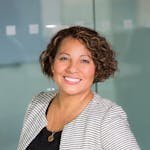 A confident woman with curly hair smiling in an office environment, conveying professionalism and approachability.